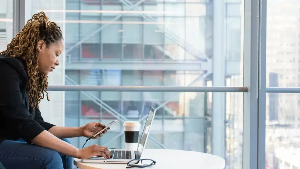 Focused woman in a black shirt using a laptop and smartphone in a high-rise, representing med spa owners enhancing their online presence with healthcare website development and design services.