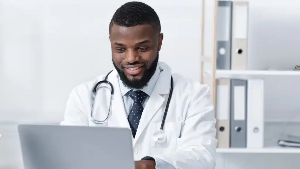 Smiling doctor in a white coat typing on a computer. Represents medical spa SEO agency solutions, digital marketing for chiropractors, social media marketing ideas for dentists, and strategies from top healthcare marketing agencies.