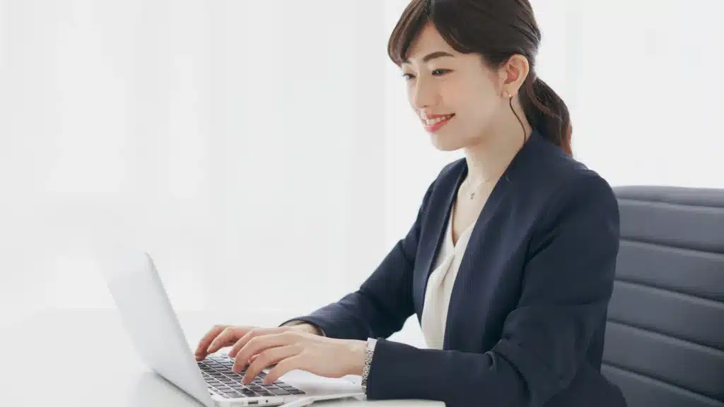 A professional woman in business attire smiles while typing on a computer at her desk. The clean, modern setting represents professionalism and strategy for med spa websites. Image conveys med spa digital marketing, med spa advertising, and med spa marketing strategies for business growth.